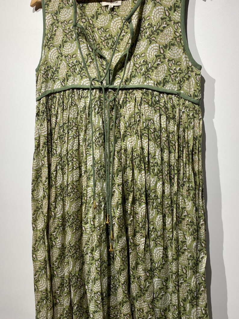 May include: Sleeveless green dress with a floral pattern in white and green. The dress features a V-neckline with a drawstring and a gathered skirt. The trim and drawstring are a darker shade of green.
