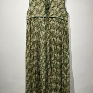 May include: Sleeveless green dress with a floral pattern. The dress has a round neckline, a drawstring detail at the chest, and a pleated skirt. The dress is hanging on a wooden hanger.