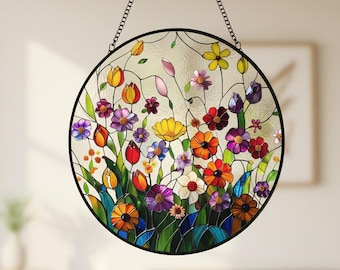 May include: A round stained glass window with a black metal frame and chain. The window features a colorful floral design with red, orange, yellow, purple, and white flowers. The glass is clear, allowing light to pass through.