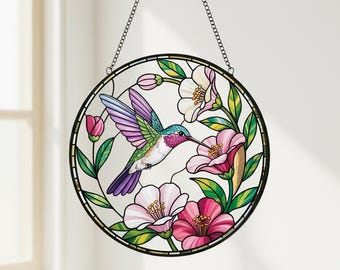 May include: A round stained glass window featuring a hummingbird and flowers. The hummingbird has purple, green, and blue feathers, with a long beak. Pink and white flowers and green leaves surround the bird. The window is framed in black and hangs from a chain.