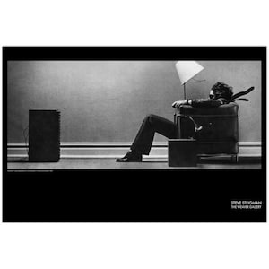May include: Black and white photograph of a person reclining in a leather armchair, with a lamp and speaker in the background. The image is a portrait of a person in a room. The photograph is signed by Steve Steigman.