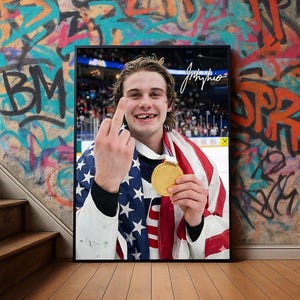 May include: Framed print featuring a smiling person holding a gold medal and draped in an American flag. The person is giving the middle finger. The background is a wall with graffiti art.
