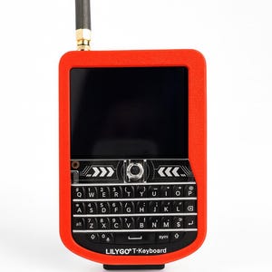 Op de afbeelding: Een draagbaar elektronisch apparaat met een feloranje rechthoekige behuizing, een zwart QWERTY-toetsenbord en een zwarte antenne. Het scherm is donker en het apparaat heeft de tekst LILYGO T-Keyboard in het wit onderaan gedrukt.