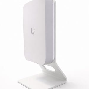 Könnte beinhalten: Ein weißes elektronisches Gerät mit einem abgerundeten rechteckigen Gehäuse und einer grauen Umrandung, montiert auf einem weißen Ständer. Das Gerät hat ein kleines, stilisiertes "U"-Logo auf der Vorderseite. Der Ständer hat eine rechteckige Basis und eine gebogene Halterung.