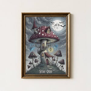 May include: A framed art print featuring a whimsical mushroom house with a spiral staircase, surrounded by smaller mushroom figures. The artwork has a dark, fantastical theme, with a sad-faced moon and the text "STAY ODD" at the bottom.