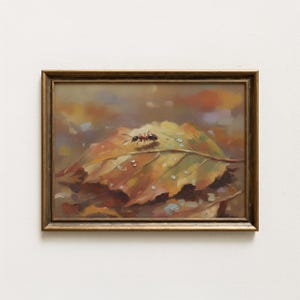 以下が含まれることがあります： 秋色の落ち葉をクローズアップで描いた額入りの油絵。葉には葉脈が見え、水滴とアリが描かれています。絵は金色のフレームに入っています。