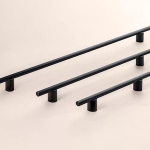 Op de afbeelding: Drie zwarte kastgrepen van verschillende lengtes. De grepen zijn cilindrisch met een stanggreep en een ronde basis. De langste greep is ongeveer 40 cm lang, de middelste 25 cm en de kortste 15 cm.