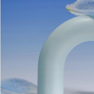 Op de afbeelding: Een lichtblauwe, boogvormige sculptuur met een matte afwerking, tegen een blauwe achtergrond. Een delicate, doorschijnende bloemblaadje rust op de boog, met een ander aan de basis. De compositie roept rust op.