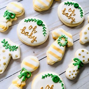 Puede incluir: Un conjunto de nueve galletas decoradas con tem&aacute;tica de baby shower. Las galletas est&aacute;n decoradas con glaseado dorado y verde y presentan dise&ntilde;os como un sonajero, un mameluco y la frase "Oh Baby".