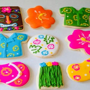 May include: A collection of nine decorated sugar cookies featuring tropical themes, including a brown tiki mask, orange and pink hibiscus flowers, green and blue button-down shirts, a white circular cookie with floral patterns, flip-flops, and a hula skirt.