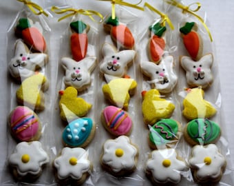 May include: Easter-themed cookies in clear cellophane bags tied with yellow ribbons. The cookies include carrots, bunnies, chicks, decorated eggs, and flowers. The cookies are decorated with white, pink, blue, yellow, orange, and green icing.