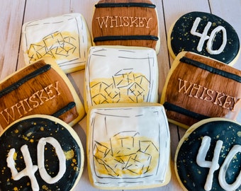 May include: A set of nine decorated sugar cookies. The cookies are decorated with a whiskey theme. Some cookies are shaped like barrels with the word "Whiskey" written on them. Other cookies are shaped like glasses with ice cubes and the number "40" on them. The cookies are decorated with brown, black, white, and gold icing.