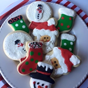 May include: A plate of Christmas-themed sugar cookies decorated with white, red, and green icing. The cookies feature designs of snowmen, Santa Claus, and stockings.