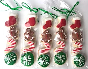 May include: Five clear plastic bags each containing four holiday-themed sugar cookies: a red stocking, a brown gingerbread person, a red and white candy cane, and a green snowflake cookie. Each bag is tied at the top with a thin green ribbon.
