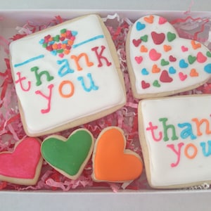 May include: A gift box filled with colorful cookies decorated with the words "thank you". The cookies are in the shape of hearts and squares.
