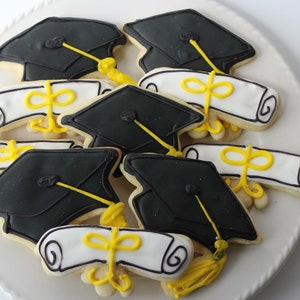 Op de afbeelding: Een bord met afstudeer-suikerkoekjes versierd met zwart en wit glazuur. De koekjes zijn gevormd als afstudeerhoeden en diploma's.