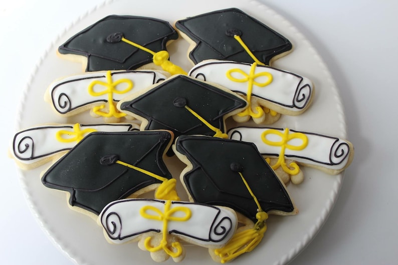 Op de afbeelding: Een bord met afstudeer-suikerkoekjes versierd met zwart en wit glazuur. De koekjes zijn gevormd als afstudeerhoeden en diploma's.