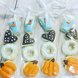 May include: Four clear plastic bags filled with various decorated sugar cookies. The cookies are in the shapes of hearts, donuts, coffee cups, and pumpkins. The cookies are decorated with blue, white, brown, and orange icing.