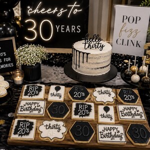 May include: A 30th birthday party display featuring a white cake with black drip icing and a hello thirty topper, surrounded by black and white cookies with text like RIP 20's and Happy Birthday, plus cake pops and signage reading cheers to 30 years.