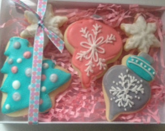 May include: Assortment of Christmas-themed sugar cookies decorated with blue, white, and pink frosting. The cookies are shaped like a star, a snowflake, a Christmas tree, and an ornament.