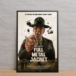 以下が含まれることがあります： スタンリー・キューブリック監督の映画「フルメタル・ジャケット」の額入りポスター。ポスターには、軍服姿の男性が視聴者を指さし、背景にはヘリコプターと兵士が描かれています。タイトルが大きく表示されています。
