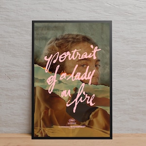 以下が含まれることがあります： 「燃える女の肖像」の映画ポスター。女性の顔が、破れた炎のイメージで部分的に隠されています。ピンク色の文字で映画のタイトルが書かれています。ポスターは黒いフレームに入っています。