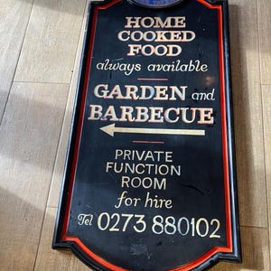Könnte beinhalten: Schwarzes rechteckiges Schild mit rotem Rand. Der Text wirbt für "HOME COOKED FOOD", "GARDEN and BARBECUE" und "PRIVATE FUNCTION ROOM for hire". Eine Telefonnummer ist ebenfalls angegeben. Das Schild hat eine dekorative Oberseite.