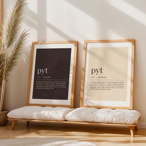 Könnte beinhalten: Zwei gerahmte Kunstdrucke mit dem Wort „pyt“ in einer modernen Schriftart. Ein Druck hat einen schwarzen Hintergrund, der andere einen beigen Hintergrund. Beide Drucke haben eine Definition unter dem Wort. Die Drucke werden auf einer Holzbank mit einem weißen Kissen ausgestellt.
