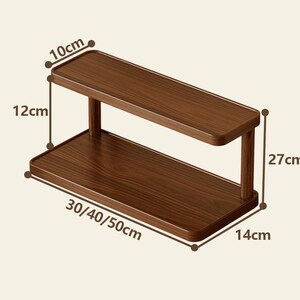May include: A two-tier rectangular wooden shelf with a dark brown wood grain finish. The shelf features a top tier measuring 10 cm deep, a 12 cm vertical clearance, and a total height of 27 cm. The base width is labeled as 30, 40, or 50 cm, with a 14 cm depth.