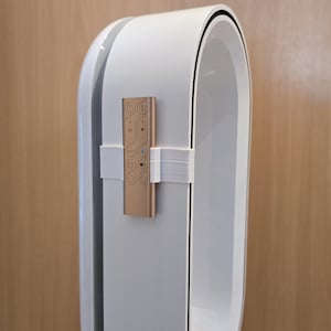 Könnte beinhalten: Ein weiß-silberner Luftreiniger mit einer goldenen Fernbedienung. Der Luftreiniger hat ein schlankes, modernes Design mit einer geschwungenen Form und einer schwarzen Umrandung. Die Fernbedienung hat mehrere Tasten.