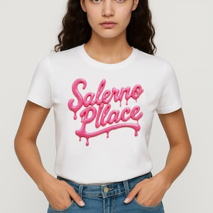 Könnte beinhalten: Weißes T-Shirt mit dem Text "Salerno Place" in einer tropfenden rosa Schrift. Das T-Shirt hat kurze Ärmel. Das Model trägt das T-Shirt und eine blaue Jeans.