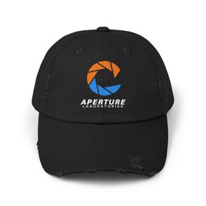 May include: Black distressed baseball cap with the Aperture Laboratories logo in orange and blue. The logo is a stylized aperture shape, with the text "APERTURE LABORATORIES" below it in white. The cap has a curved peak and a distressed finish.
