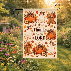 May include: A rectangular garden flag featuring the text Give Thanks To the LORD Psalm 136:1. The design includes orange pumpkins, white geese wearing leopard print bows, brown boots filled with autumn leaves, sunflowers, and scattered fall foliage.