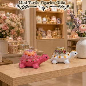 Peut inclure: Deux figurines de tortue en céramique, une rose et une blanche, ornées de motifs à pois complexes de style mandala sur leurs carapaces. Le texte 'Mini Turtle Figurine Gifts' est affiché en haut au centre au-dessus des deux petites sculptures.