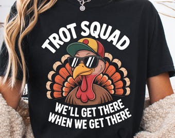 May include: Black t-shirt featuring a turkey wearing sunglasses and a baseball cap. The text on the shirt says "TROT SQUAD" above the turkey and "WE'LL GET THERE WHEN WE GET THERE" below.