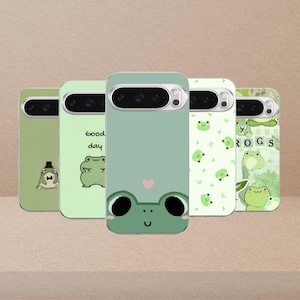 May include: Five green phone cases with frog designs. One case has a frog wearing a hat, another says "good day" with a frog, and a third has a frog face with a heart. The other two cases have frog and leaf patterns.