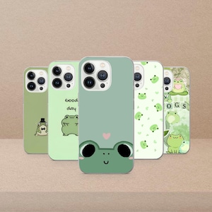 May include: Five green phone cases with frog designs. One case has a frog face with a pink heart, another says "Good day" with a frog, and another has a frog wearing a hat. The cases are for a smartphone.
