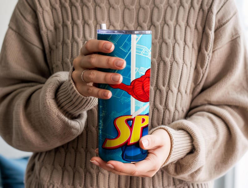 Pu&ograve; includere: Un bicchiere blu e bianco con un design da supereroe con la scritta "SP" in giallo e rosso. Il bicchiere ha una grafica a braccio rosso e una cannuccia bianca. Il bicchiere &egrave; tenuto da una persona che indossa un maglione beige.