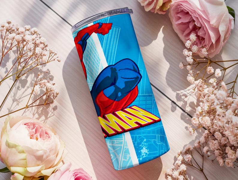 Pu&ograve; includere: Un bicchiere in acciaio inossidabile blu con un design da supereroe. Il design include una figura rossa e blu con la parola "MAN" in giallo. Lo sfondo presenta un paesaggio urbano. Il bicchiere &egrave; cilindrico e ha un coperchio trasparente.