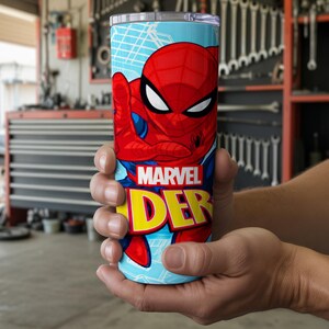 Pu&ograve; includere: Un bicchiere cilindrico con Spider-Man. Il bicchiere ha uno sfondo azzurro con una grafica di Spider-Man rossa e blu. Le parole "MARVEL" e "DER" sono in giallo e rosso. Il bicchiere &egrave; tenuto tra le mani di una persona.