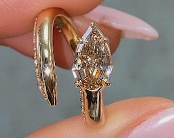 Puede incluir: Un pendiente dorado con una gema facetada en forma de pera. El pendiente tiene un diseño curvo con pequeñas piedras transparentes a lo largo de la curva. La gema es de color marrón claro y está engastada en metal dorado.