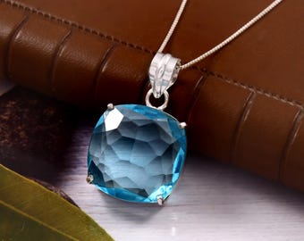 May include: A square, faceted, light blue gemstone pendant necklace. The pendant is set in a silver-colored metal and hangs from a delicate silver chain. The gemstone has a gradient of blue hues, with darker shades at the center.