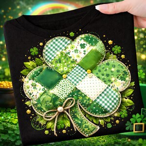 May include: Black t-shirt featuring a large, detailed shamrock design. The shamrock is composed of various green patterned fabrics, including gingham and floral prints, with a bow at the bottom. Small yellow buttons and gold accents add detail.