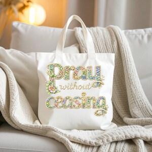 May include: A white tote bag with the embroidered phrase "Pray without ceasing" in colorful floral lettering. The bag has two handles and is made of a sturdy fabric, perfect for carrying books or groceries.