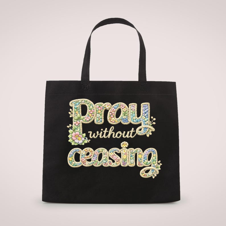 May include: Black tote bag with the words "Pray without ceasing" in colorful, floral-style lettering. The bag has two black handles and a simple design, suitable for carrying various items.