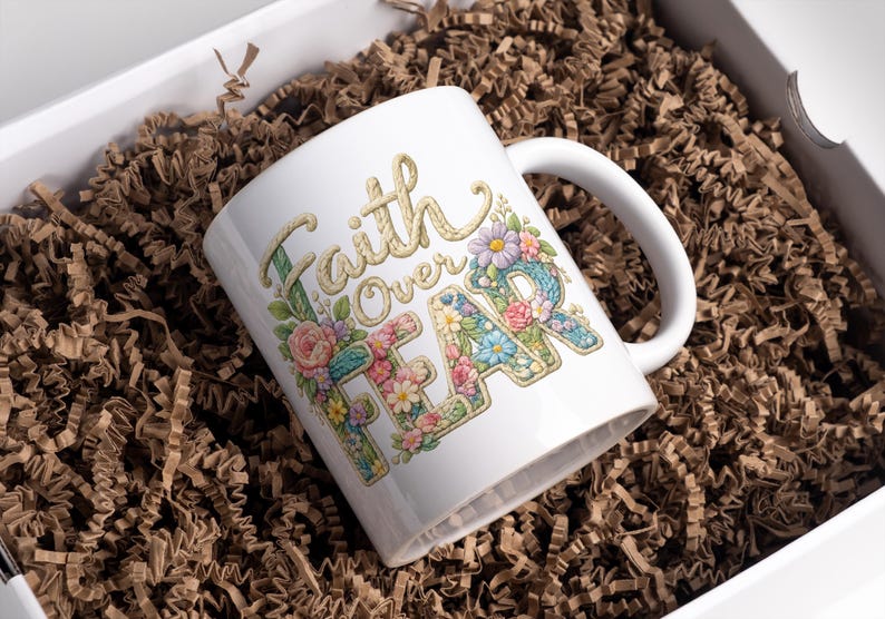 May include: White ceramic mug with the words "Faith Over Fear" in a floral design. The mug is decorated with colorful flowers and is presented in a white gift box with brown paper filler.