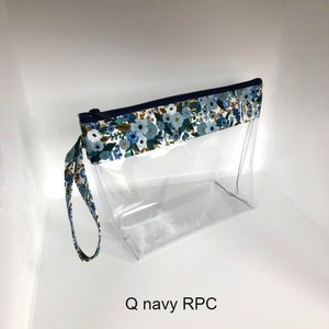 May include: A clear, rectangular cosmetic bag with a navy blue zipper and a floral patterned trim. The trim features blue and white flowers on a white background. A matching patterned wrist strap is attached. The text "Q navy RPC" is visible.