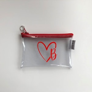 May include: Clear plastic zippered pouch with a red heart and the letter "B" inside the heart. The pouch has a red zipper and a small white tag that says "B. He Plans".