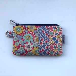 May include: A small, floral patterned coin purse with a zipper closure and a key ring. The purse features a colorful design with red, blue, yellow, and white flowers. The tag on the side reads "B Hip Bags".