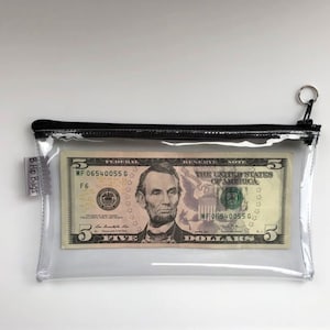 May include: A clear plastic zippered pouch with a black zipper and a black trim. The pouch contains a five dollar bill with the portrait of Abraham Lincoln. The pouch has a label that reads "B. Hip Bags".